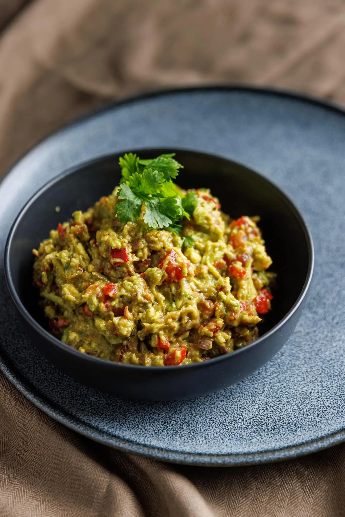 A bowl of fresh chunky guacamole with tortilla chips, avocados, and limes in the background.