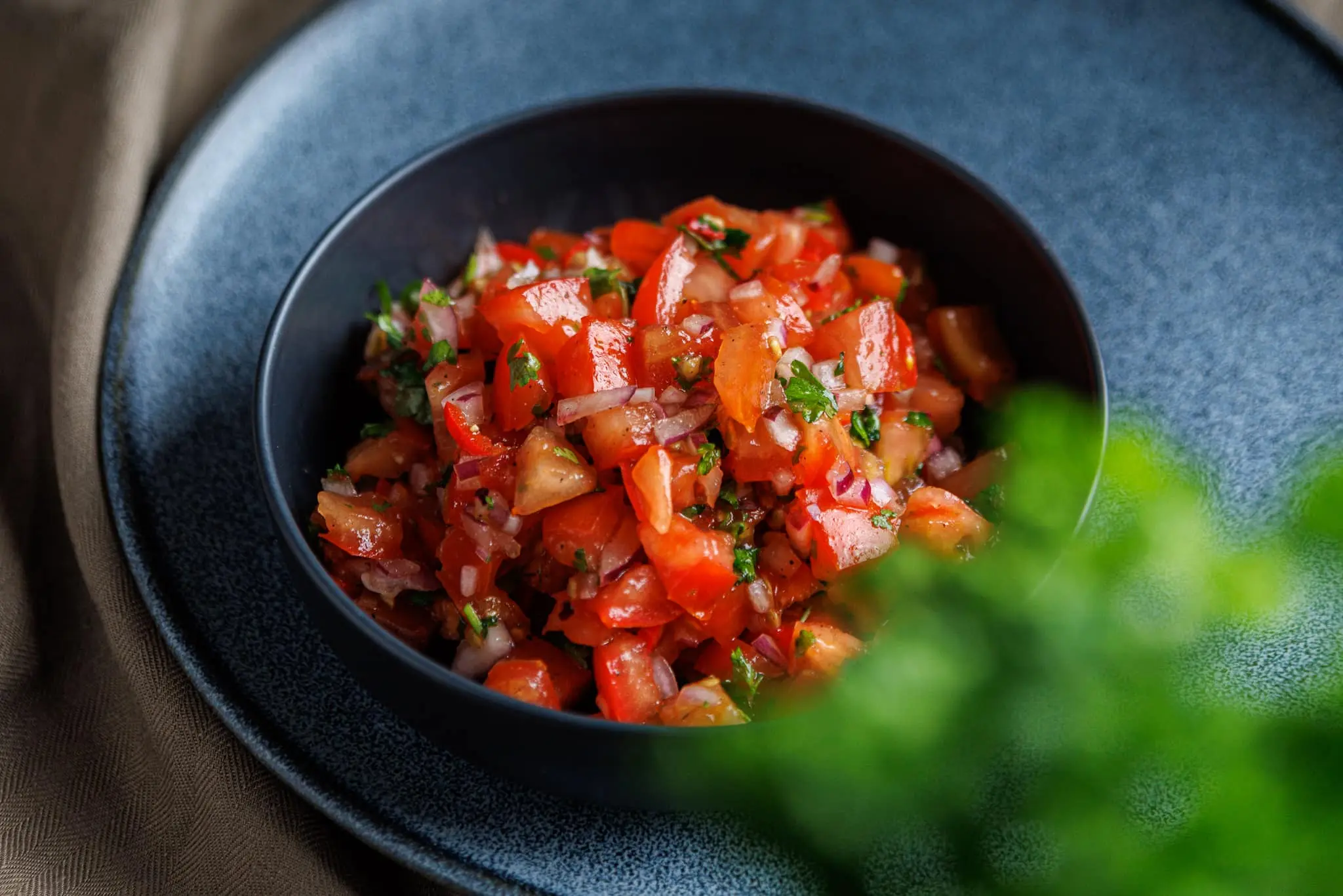 A dark serving bowl filled with fresh, homemade pico de gallo salsa showing diced tomatoes, red onions, and cilantro.